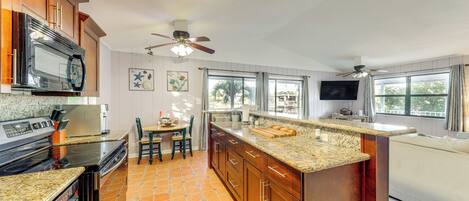 A kitchen with granite countertops, a built-in microwave, a stove, and a ceiling fan.