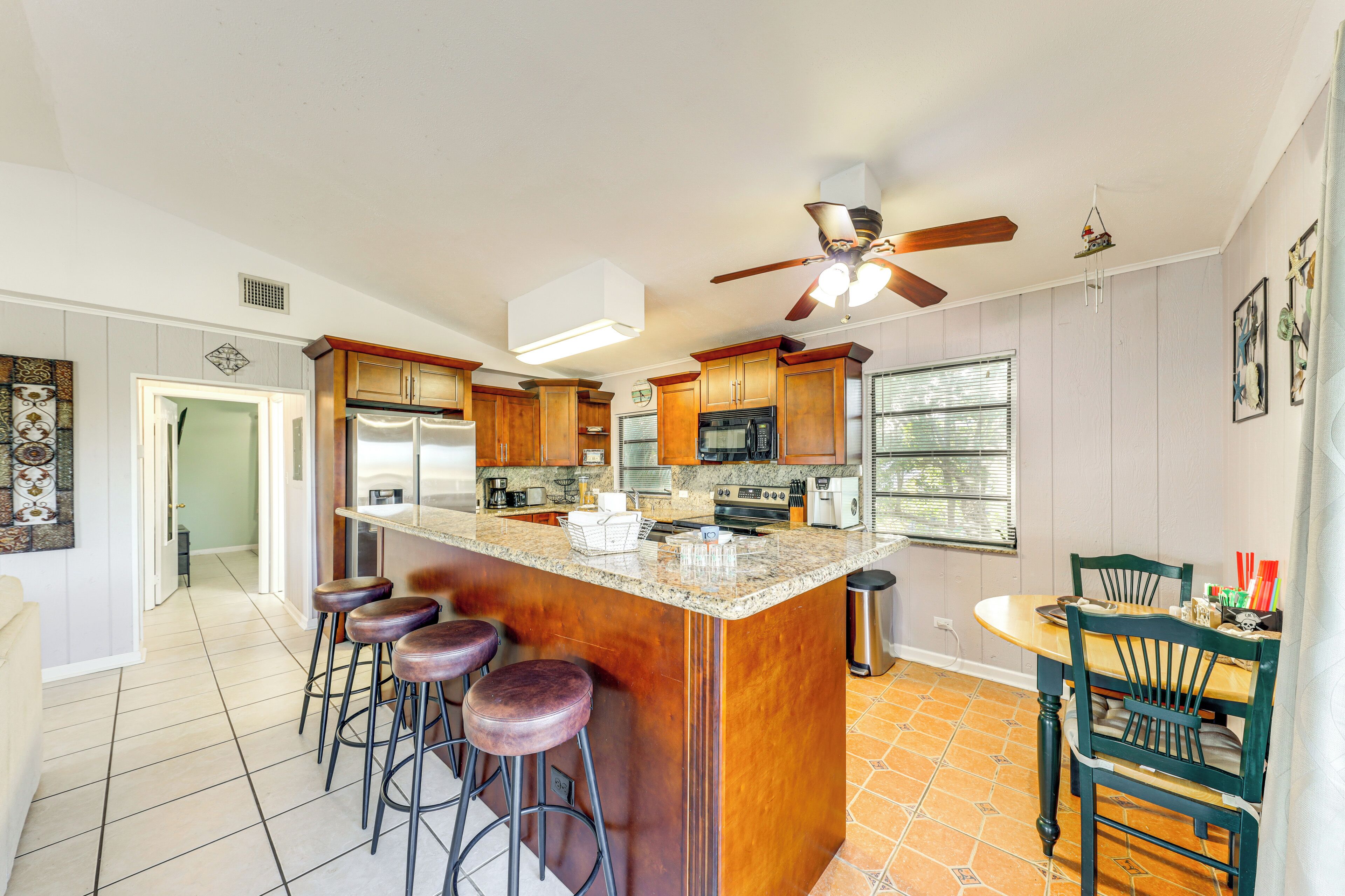 A kitchen with a central island, bar stools, wooden cabinets, a ceiling fan, and a dining area with chairs.