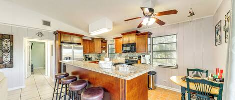 A kitchen with a central island, bar stools, wooden cabinets, a ceiling fan, and a dining area with chairs.