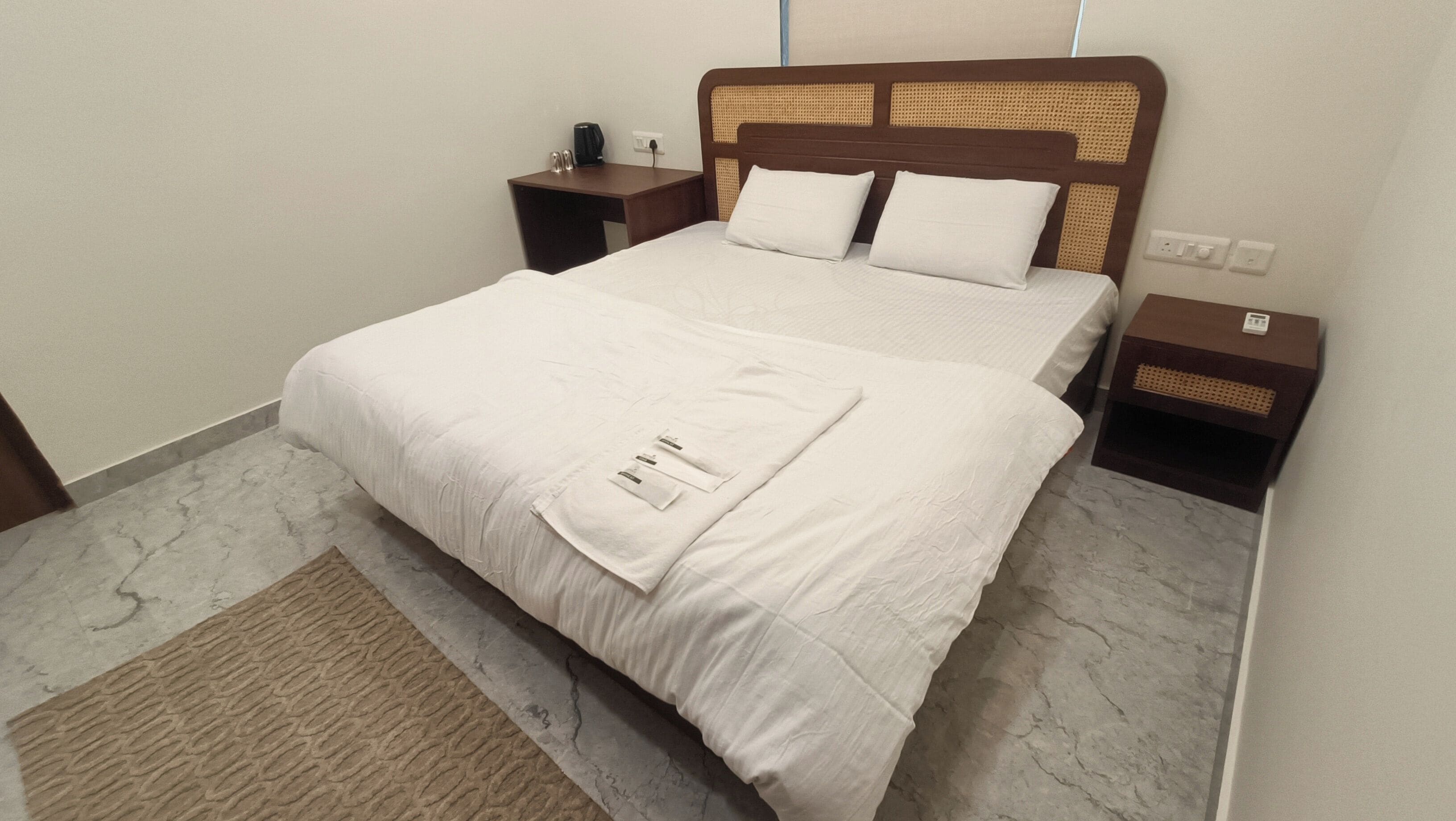 Una cama doble bien hecha con cabecera de madera, dos mesitas de noche y suelo de mármol.