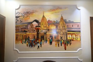 A mural of a traditional Indian architectural scene with people. - Hare Krishna Stays (Varanasi)