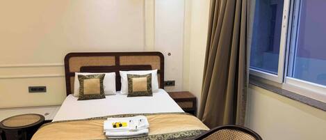 A neatly made bed with two pillows, a bedside table, a chair, and a window with curtains.