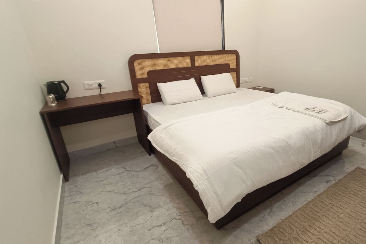 A neatly made bed with white bedding, a wooden headboard, and a bedside table with a black object on it.