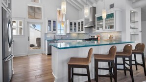 A modern kitchen with a large island, white cabinetry, and bar stools.