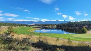 Un parcours de golf avec un lac, entouré de montagnes et d’une forêt dense.