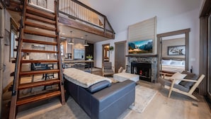 Un vaste espace de vie comprenant un salon avec une chambre en mezzanine, une cheminée et un coin repas.
