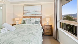 Habitación de hotel con cama, dos mesitas de noche con lámparas, un cuadro en la pared y ventana con vistas.