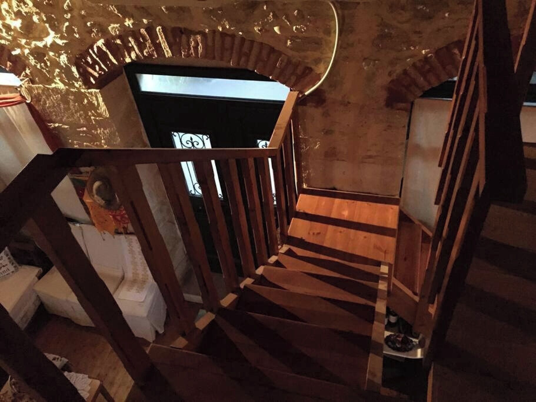 A wooden staircase with a metal railing, leading to a room with a white wall and a window.