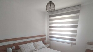 A bedroom with a bed, a nightstand, a dresser, a hanging light fixture, and a window with horizontal blinds. - House pontevedra, enjoys tranquility 5 min from the beach and 3 min from downtown  (Pontevedra)