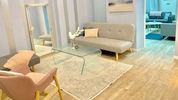 A modern living room with a sofa, a glass coffee table, a pink chair, a large mirror, and a patterned rug. - Charming, Fun, 3-Suite Apartment in Vibrant Budapest (Budapest)