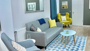 A modern living room with a grey sofa, a yellow armchair, and a rocking chair. A blue and white patterned rug is on the floor. - Charming, Fun, 3-Suite Apartment in Vibrant Budapest (Budapest)