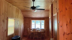 Una cabaña de madera con comedor, ventilador de techo y ventana con persianas.