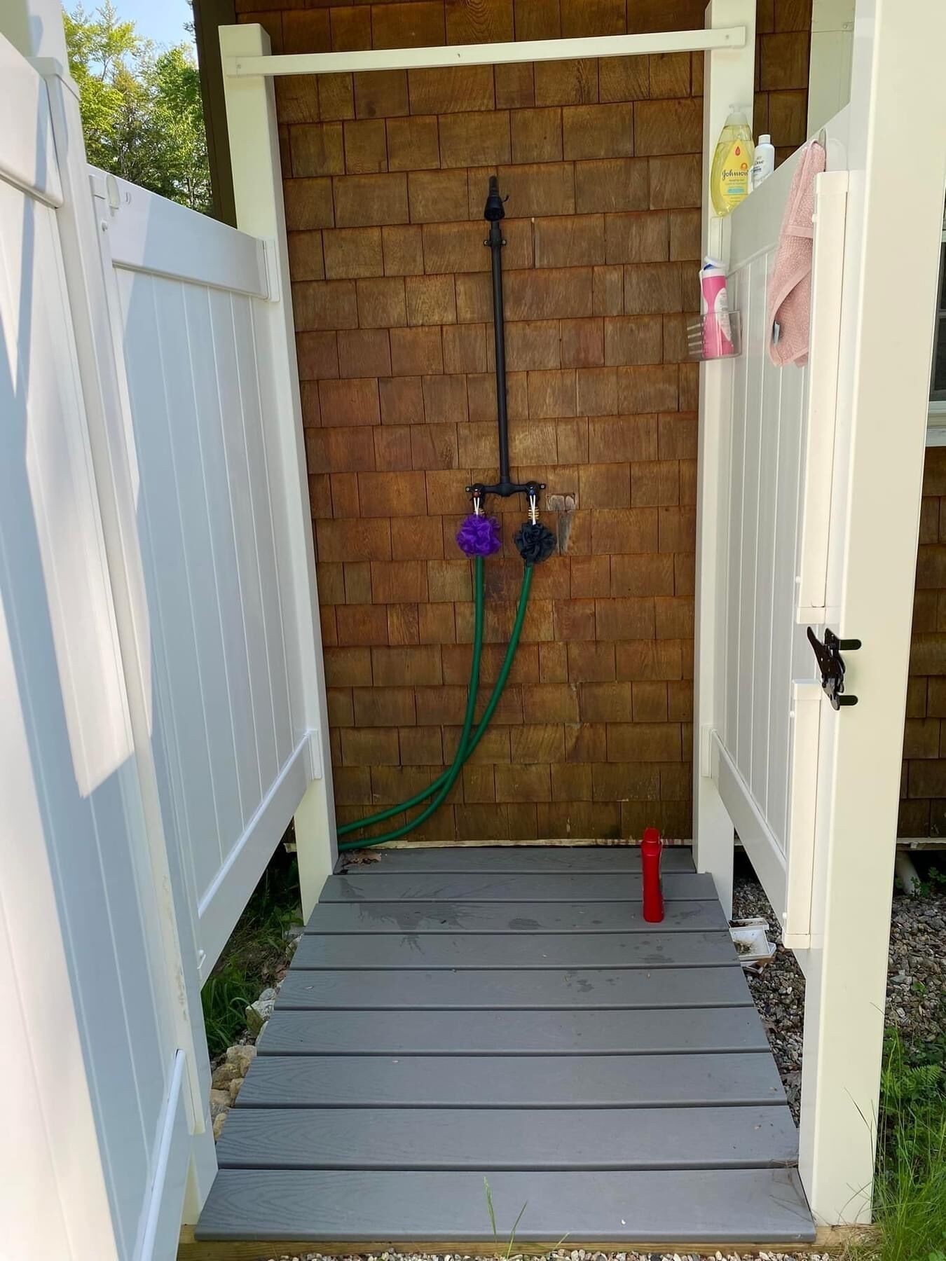 A wooden deck with a white fence, a hose, and a red object on the ground.