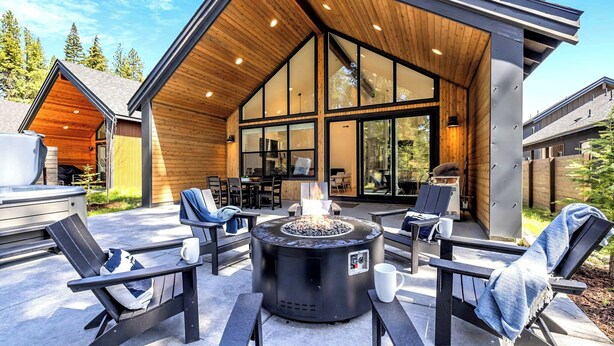 Une terrasse extérieure dotée d’un foyer, de sièges et d’une grande porte vitrée donnant sur un espace intérieur.