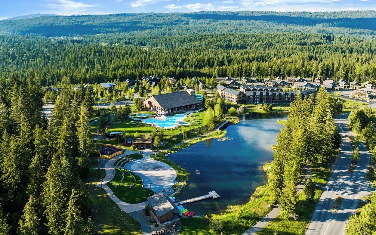 Um resort com uma grande piscina, um lago e um cenário de mata.