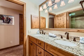Une salle de bain avec des meubles en bois, un comptoir en granit, un grand miroir et un luminaire au plafond.