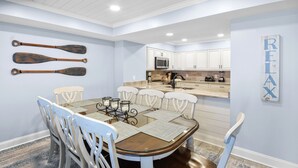 A dining area with a wooden table and white chairs, a kitchen with white cabinets and a microwave, and a 'RELAX' sign on the wall.