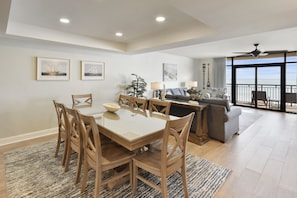 A spacious dining area with a large table and chairs, a sofa, and a balcony with a view. - Southwind 806 5 Bedroom Condo (Myrtle Beach)