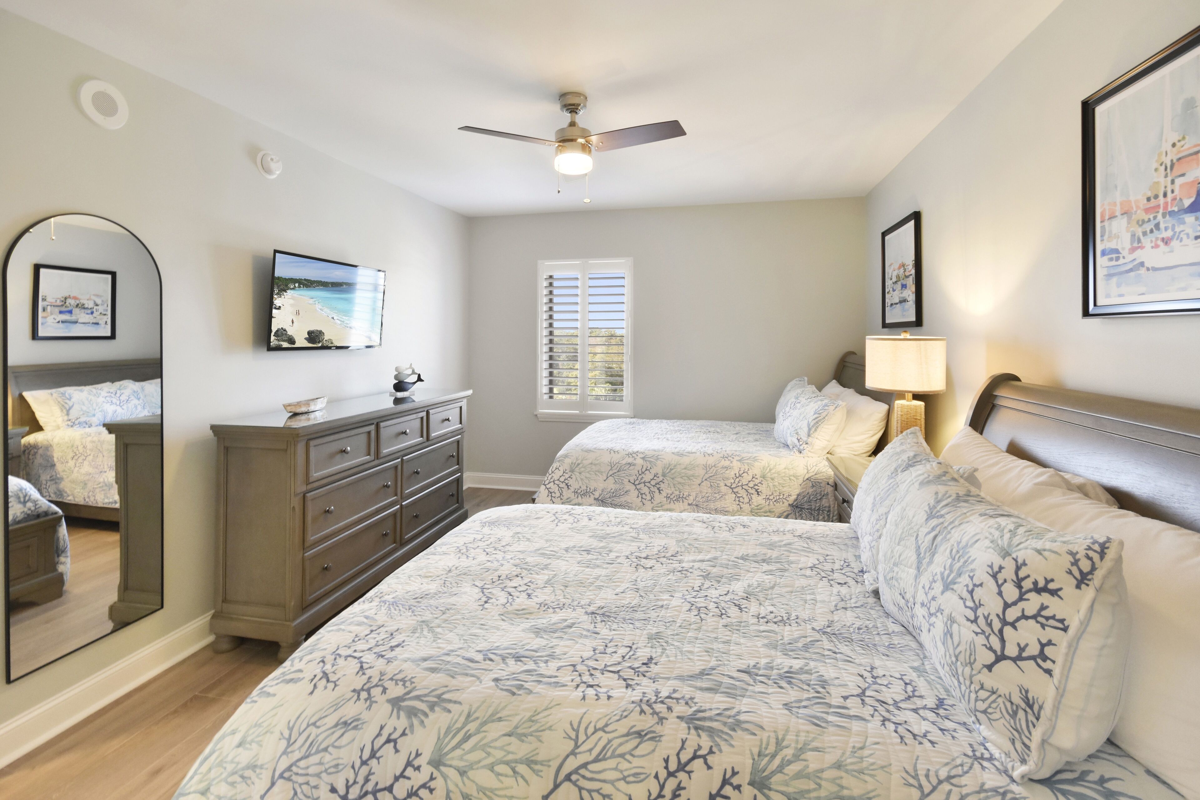 A bedroom with two beds, a ceiling fan, a dresser, and a window with blinds.