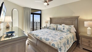 A bedroom with a large bed, a ceiling fan, a dresser, a nightstand, and a view of the outdoors. - Southwind 806 5 Bedroom Condo (Myrtle Beach)