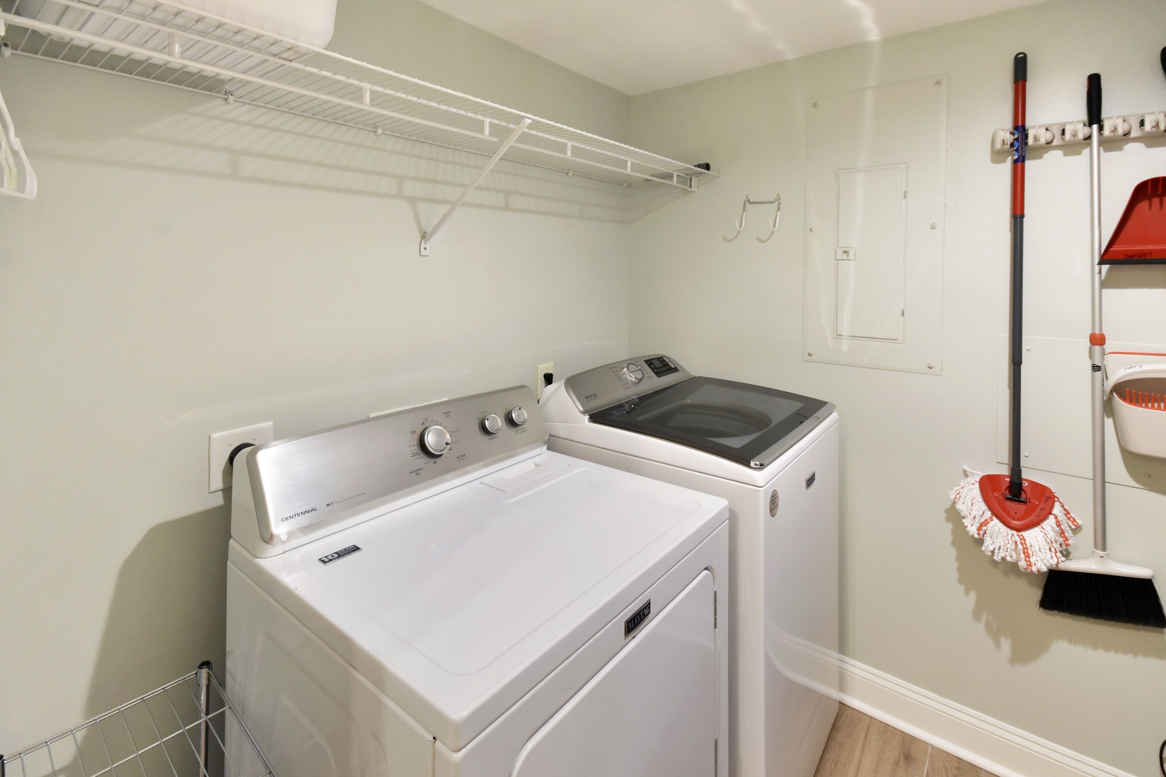 A laundry room with two washers and dryers, a metal drying rack, a broom, and a mop.
