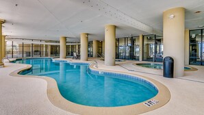 Una piscina cubierta con varias pistas, rodeada por pilares color beige y paredes de vidrio.