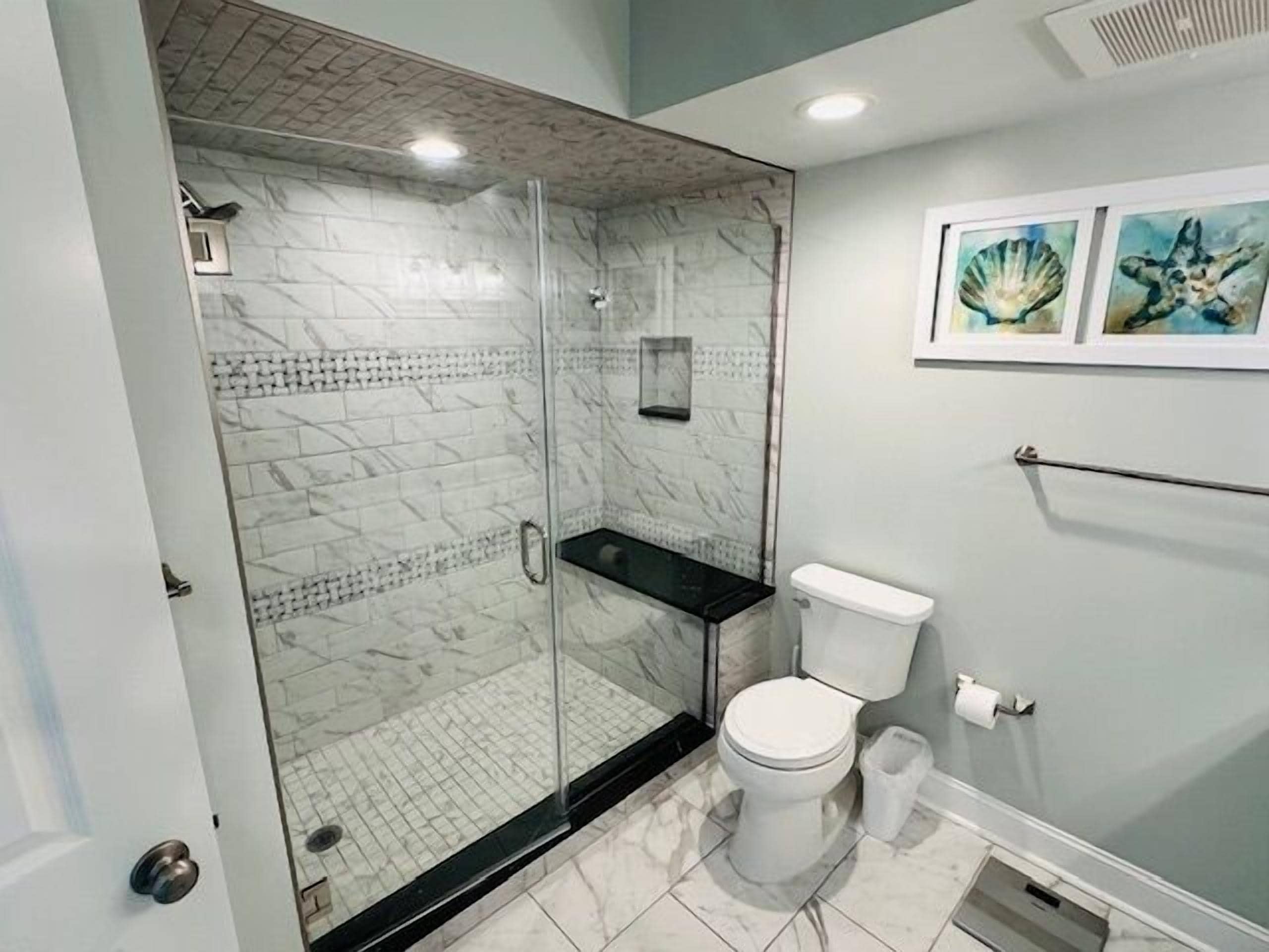 Ein Badezimmer mit einer gläsernen Duschkabine, einer weißen Toilette und einem marmorbodigen Boden.