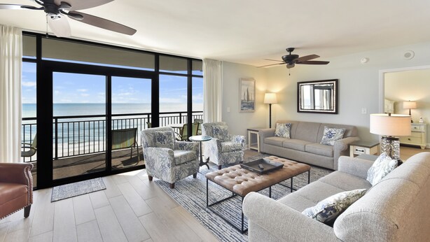 Ein geräumiges Wohnzimmer mit Balkon und Meerblick, ausgestattet mit einer Couch, Sesseln und einem Couchtisch.