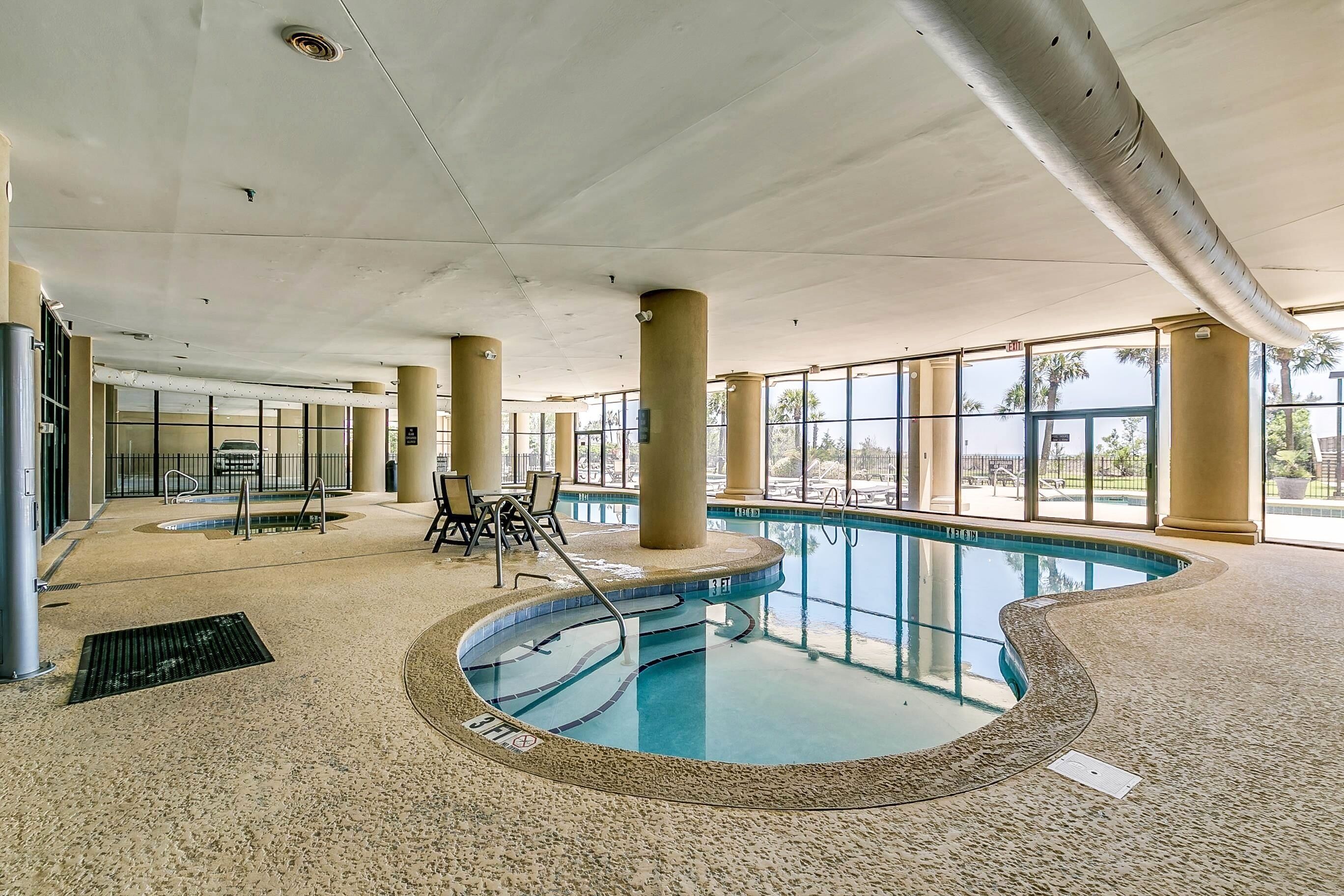Una piscina interna con vista aperta sull'esterno, circondata da ampie finestre e sostenuta da colonne.