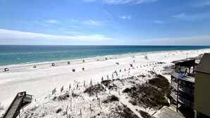 Une plage avec une promenade en bois menant à l’eau, un poste de surveillance pour les sauveteurs et un bâtiment doté de balcons donnant sur la plage.