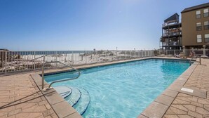 Une piscine avec vue sur la plage et l’océan, entourée d’une clôture et bordée d’un immeuble doté de balcons.