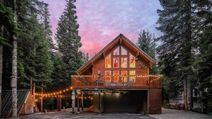 A wooden cabin with a balcony, surrounded by tall trees and a sunset sky.