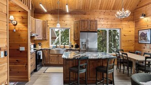 A wooden cabin interior with a kitchen, dining area, and a large window.