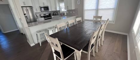 Eine moderne Küche mit weißen Schränken, einer zentralen Kochinsel und einem Essbereich mit dunklem Holztisch und weißen Stühlen.