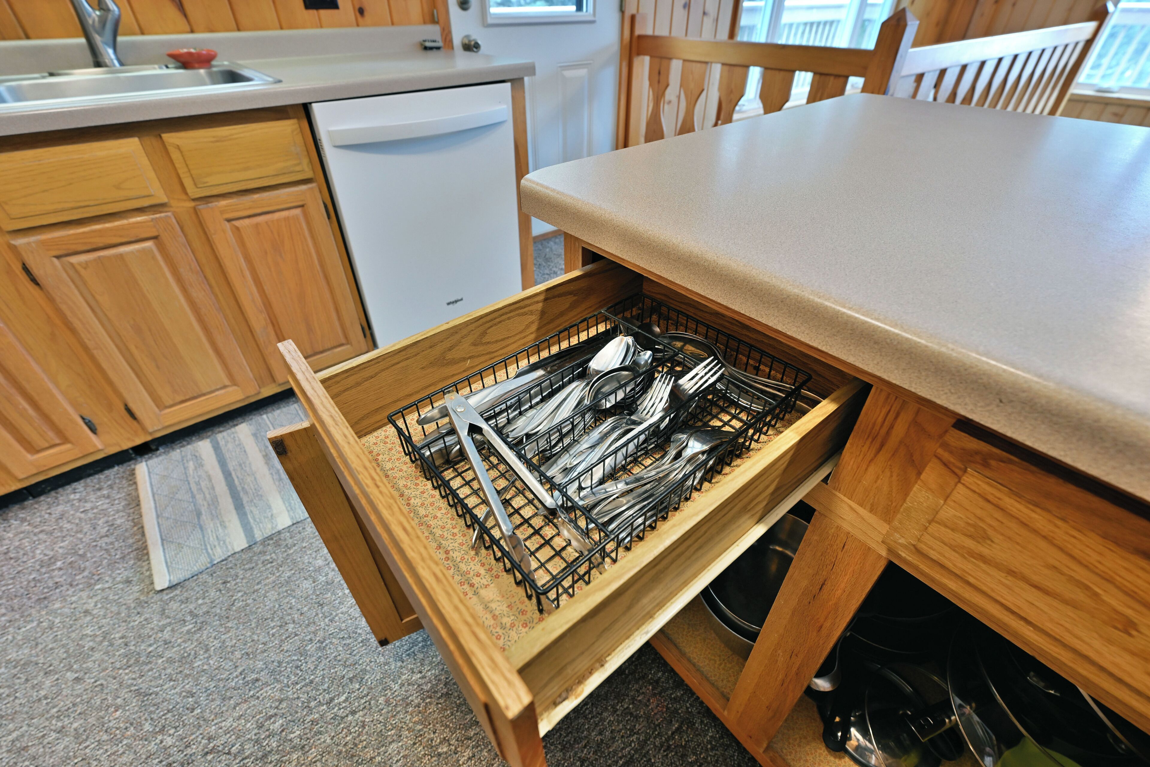 Une cuisine avec des meubles de rangement en bois, un lave-vaisselle blanc et un tiroir contenant des ustensiles.