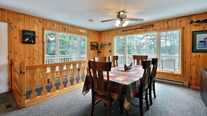 A wooden interior with a dining table, chairs, a ceiling fan, and large windows. - Lakefront Cabin with Dock, Kayaks, and Stunning Views on Quiet Teal Lake (Hayward)