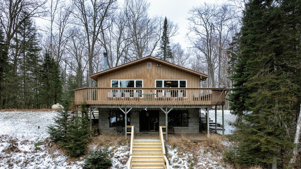 A wooden cabin with a balcony, a staircase leading to the entrance, and a snowy landscape. - Lakefront Cabin with Dock, Kayaks, and Stunning Views on Quiet Teal Lake (Hayward)