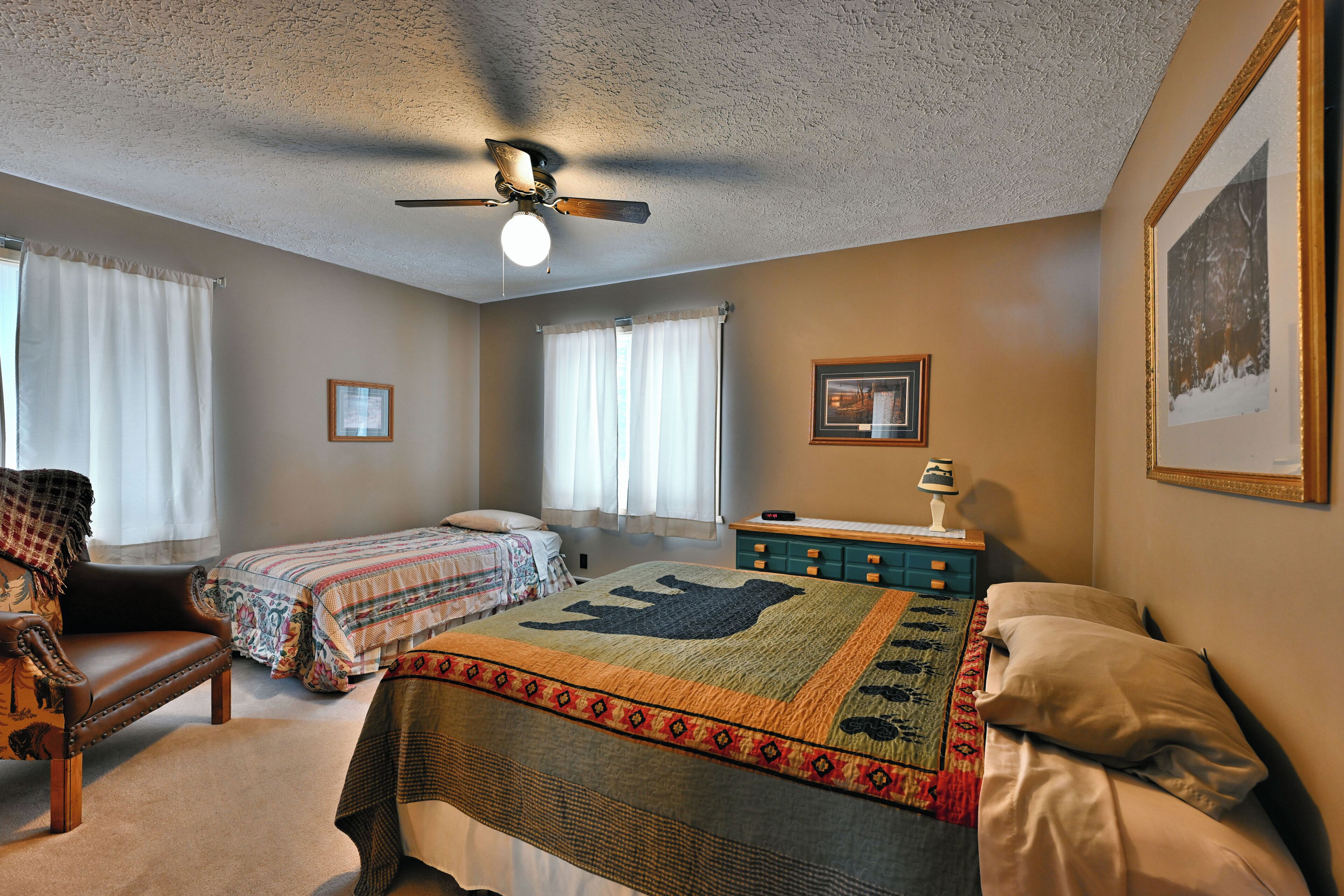 A bedroom with two beds, a ceiling fan, a dresser, and a window with curtains.