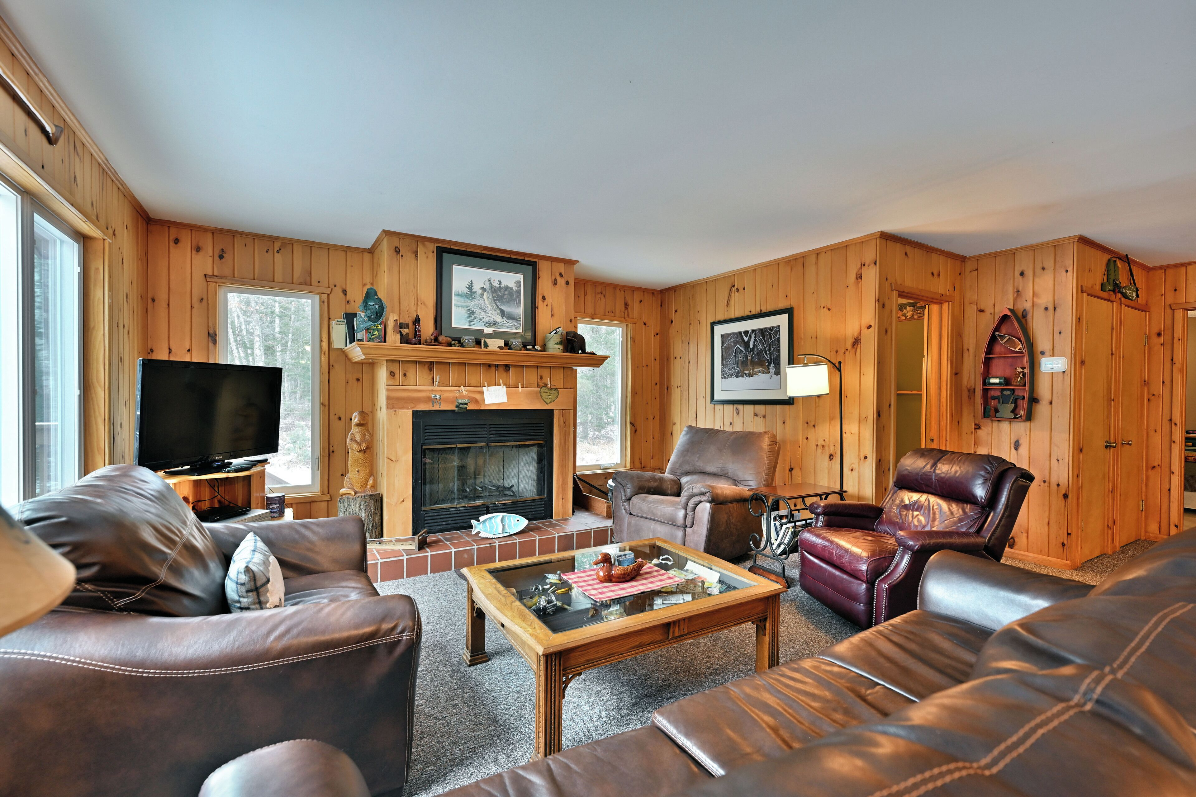 Ein gemütliches Wohnzimmer mit Ledersofas, einem Kamin, einem Fernseher und Holzvertäfelung.