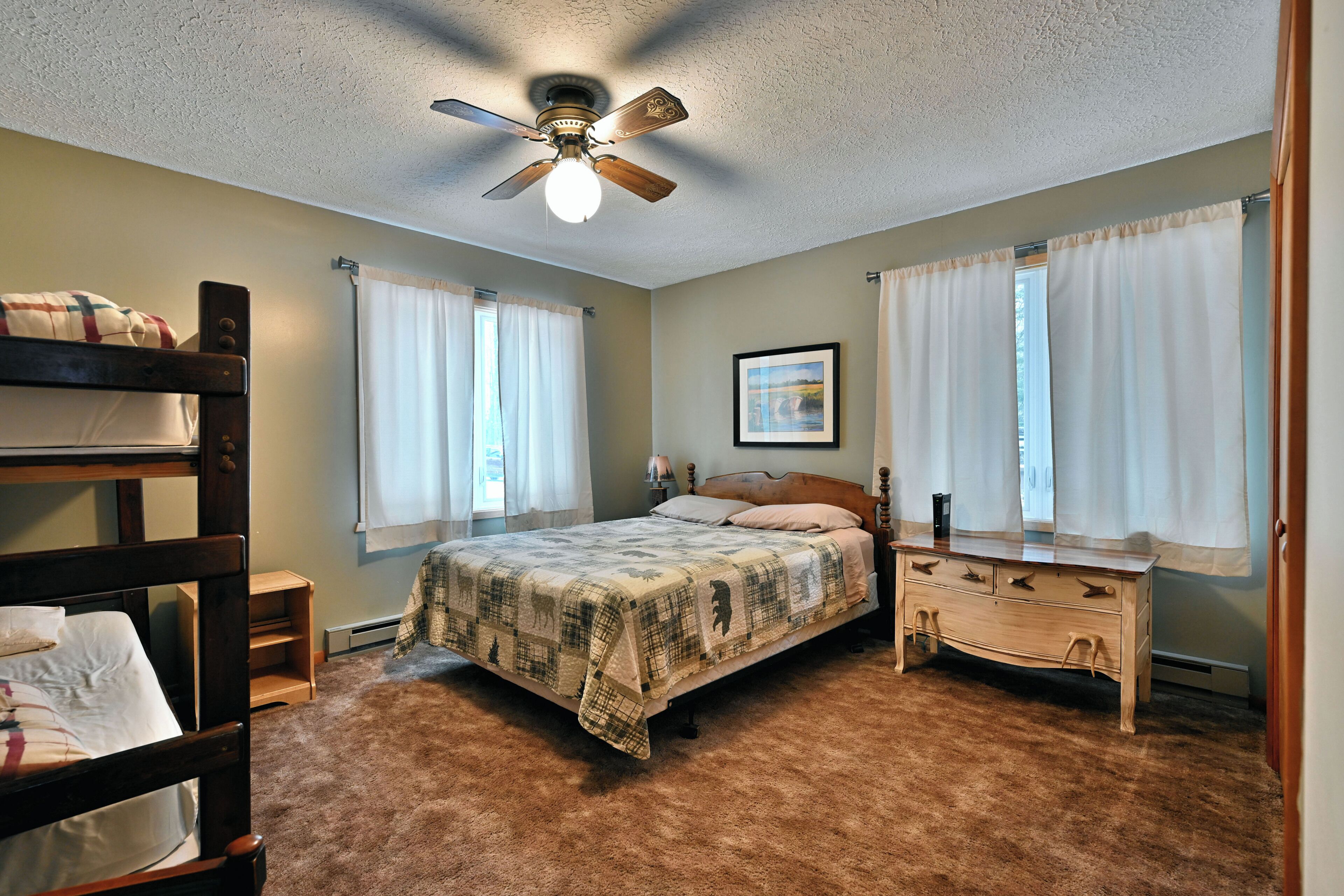 A bedroom with a bunk bed, a single bed, a wooden dresser, and a ceiling fan.