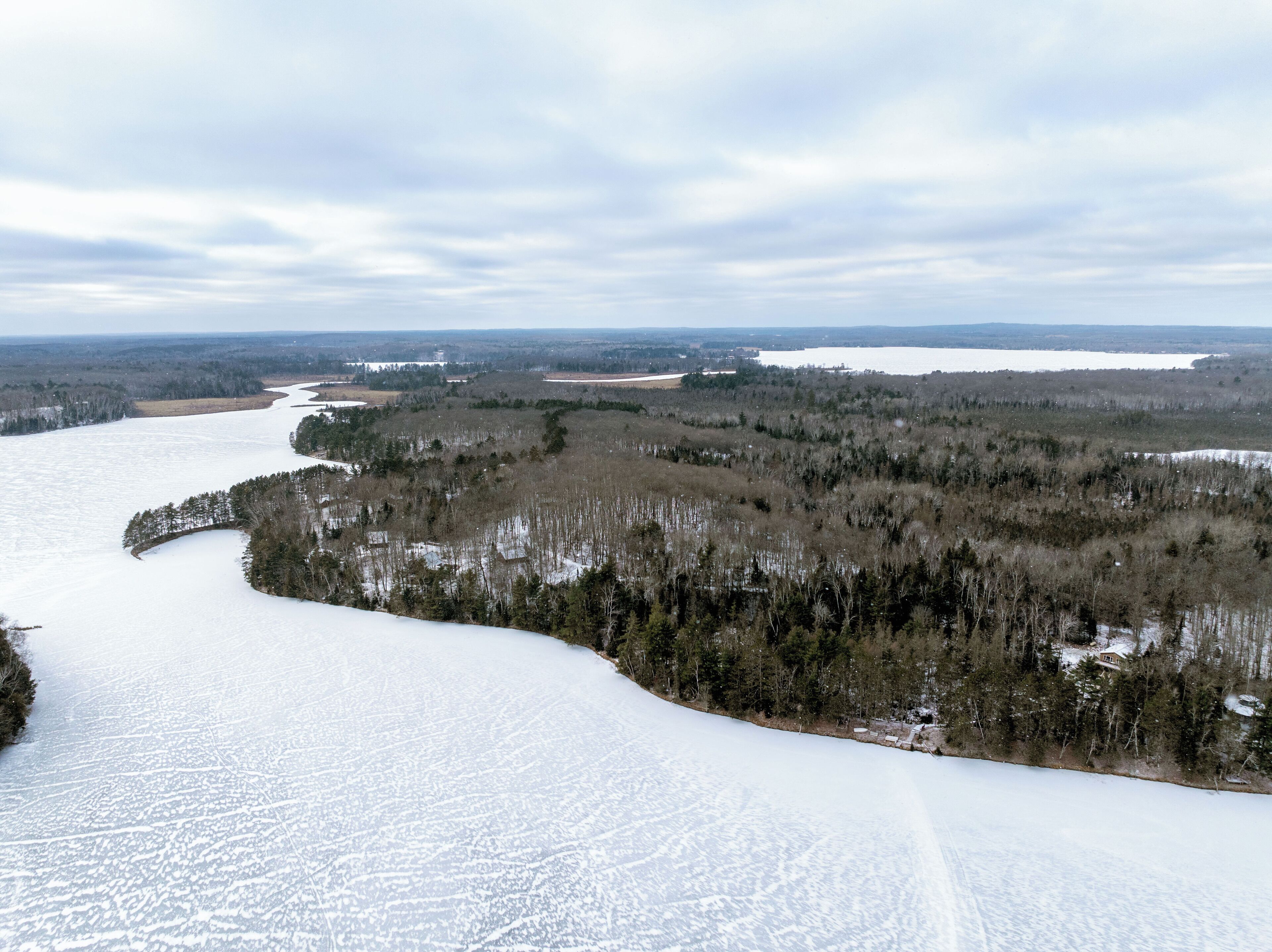 Schneebedeckte Landschaft mit Fluss, dichtem Wald und Gebäuden in der Ferne.