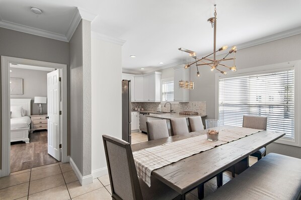 A modern kitchen with white cabinets, a dining area with a wooden table and chairs, and a chandelier.