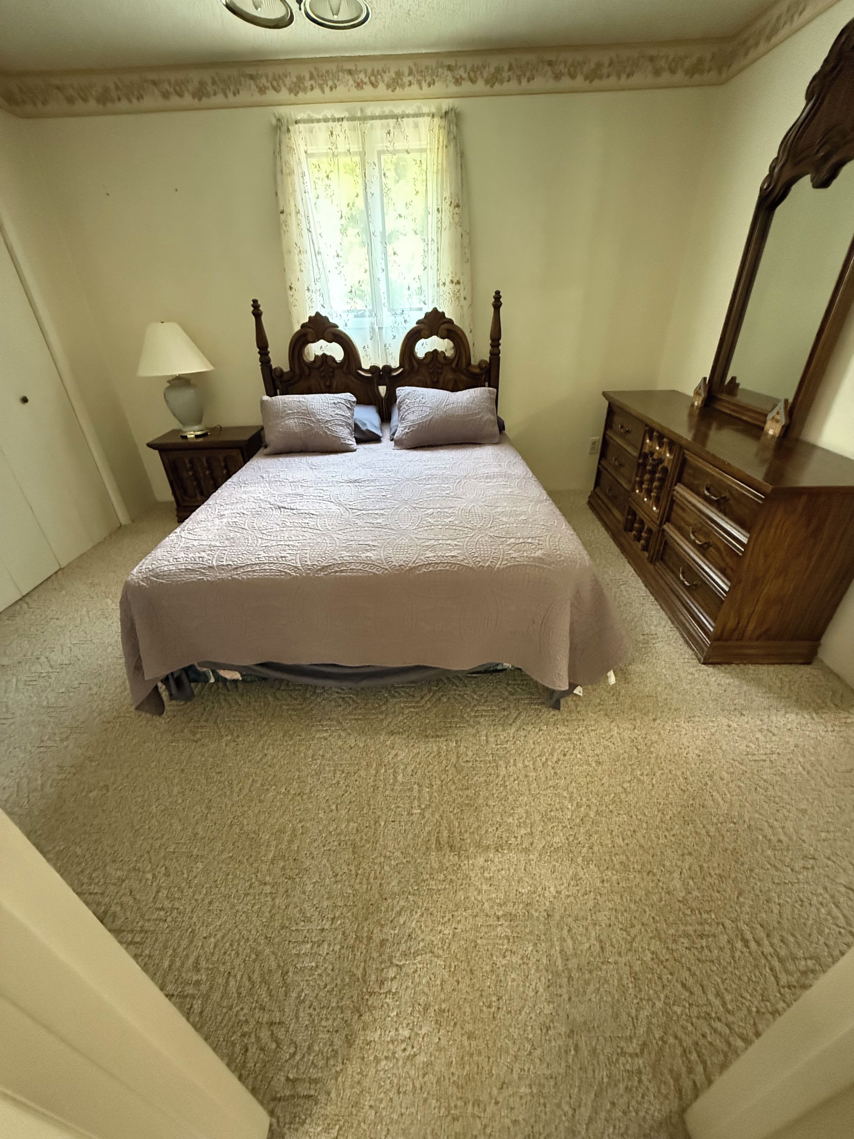 Quarto com cama, cômoda, espelho e janela com cortinas.