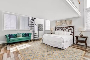 Une chambre à coucher avec un lit, un canapé vert, un escalier et un tapis à motifs.