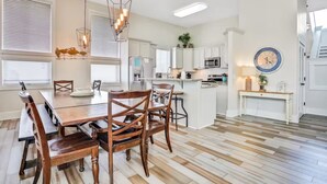 A modern kitchen with white cabinets, a wooden dining table, and a hanging light fixture. - Luxurious gulf side living with Golf Cart! + Free Dolphin Cruise! (Santa Rosa Beach)