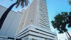A tall, modern skyscraper with a unique wavy facade, surrounded by palm trees and other greenery.