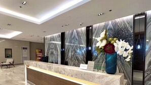 A modern reception desk with a marble counter and wooden panel, flanked by a decorative wall with a marble pattern and a large vase of flowers.
