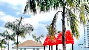 A playground with slides and red umbrellas, surrounded by palm trees and a building with a tiled roof.