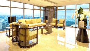 A spacious living room with a yellow sofa set, a coffee table, and a large window offering a city view.