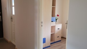 A hallway leading to a room with a wooden floor, a white door, and a small window.